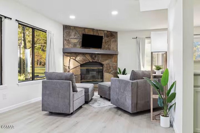 living room with a stone fireplace, a healthy amount of sunlight, and light wood-type flooring