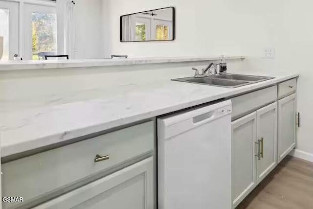 kitchen with white dishwasher, light stone countertops, sink, and hardwood / wood-style floors