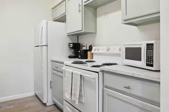 kitchen with light stone countertops, light wood-type flooring, and white appliances