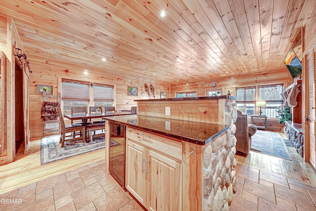 kitchen featuring a center island, light brown cabinetry, wooden ceiling, wooden walls, and dark stone counters