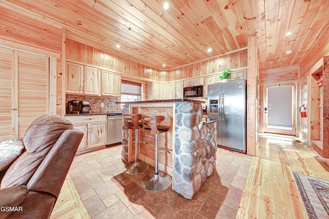 kitchen with a center island, wooden ceiling, stainless steel appliances, wood walls, and a breakfast bar area