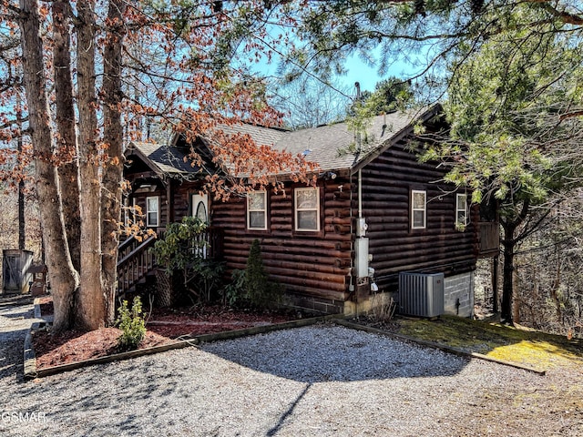 view of side of property with central AC unit, roof with shingles, and log siding