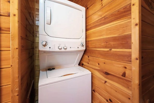 clothes washing area with stacked washer / drying machine and wood walls