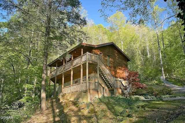 exterior space featuring a view of trees, a deck, and stairs