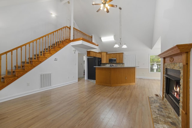 kitchen with black refrigerator, light wood-type flooring, high vaulted ceiling, and ceiling fan with notable chandelier