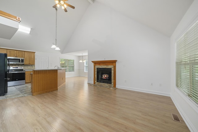 kitchen featuring a tile fireplace, light hardwood / wood-style flooring, pendant lighting, a kitchen island, and appliances with stainless steel finishes