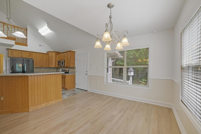 kitchen featuring lofted ceiling, black fridge, hanging light fixtures, light wood-type flooring, and a notable chandelier