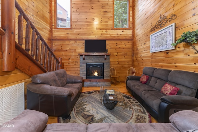 living room with wood-type flooring, a stone fireplace, and wooden walls