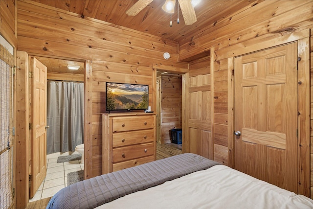 bedroom with wood walls, wooden ceiling, ensuite bath, ceiling fan, and light tile patterned flooring