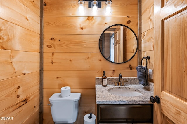 half bathroom featuring wooden walls, toilet, and vanity