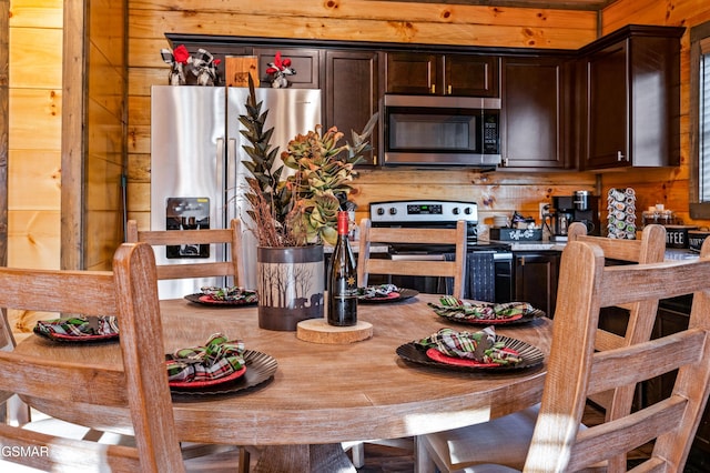 kitchen featuring stainless steel appliances, dark brown cabinets, and wood walls