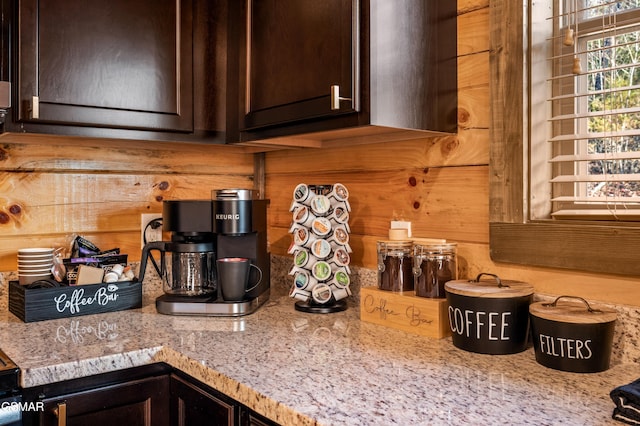 kitchen featuring wooden walls, dark brown cabinetry, and light stone countertops