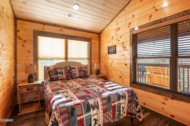 bedroom with vaulted ceiling, wood walls, wood finished floors, and visible vents