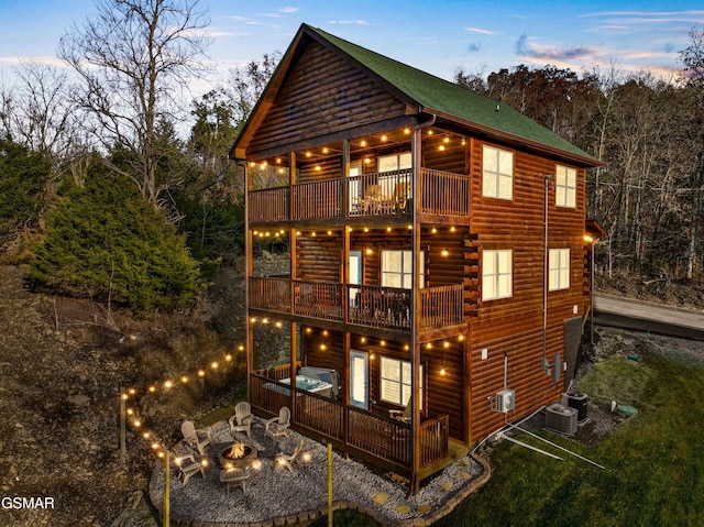 exterior space with an outdoor fire pit, log veneer siding, cooling unit, and a balcony