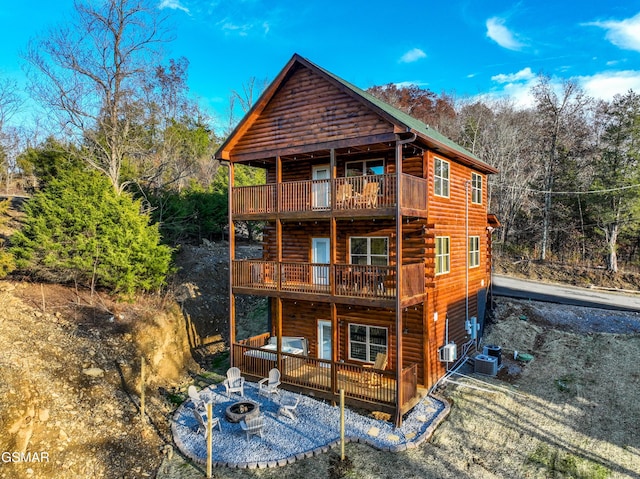 rear view of house featuring driveway, an outdoor fire pit, a balcony, and faux log siding