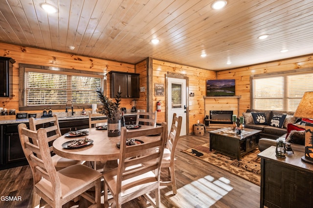 dining area featuring a warm lit fireplace, wood walls, dark wood finished floors, and wood ceiling