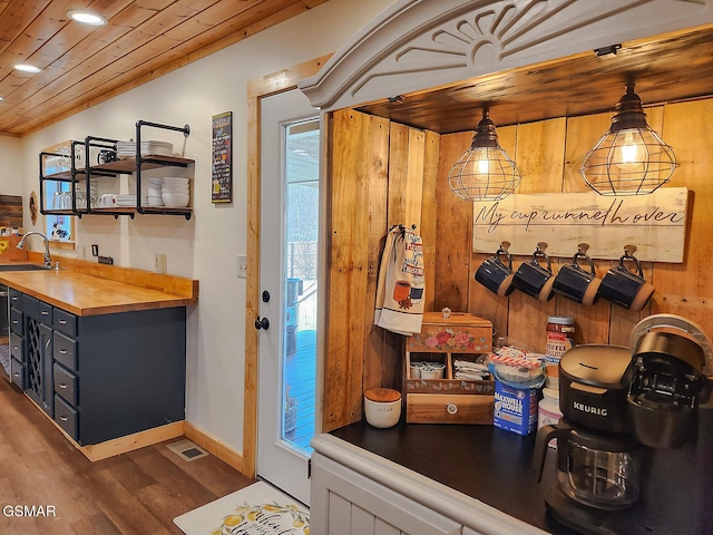 interior space featuring wooden walls, wood finished floors, baseboards, a sink, and wood ceiling