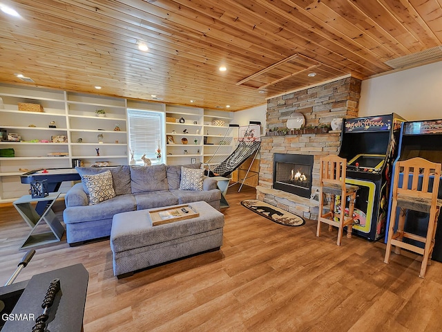 living room featuring built in features, wood finished floors, a stone fireplace, and wooden ceiling