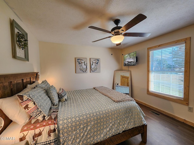 bedroom featuring visible vents, a textured ceiling, baseboards, and wood finished floors