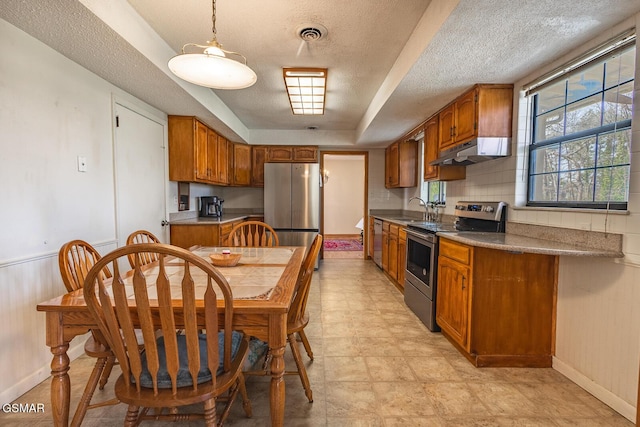 kitchen with a sink, brown cabinetry, under cabinet range hood, and stainless steel appliances