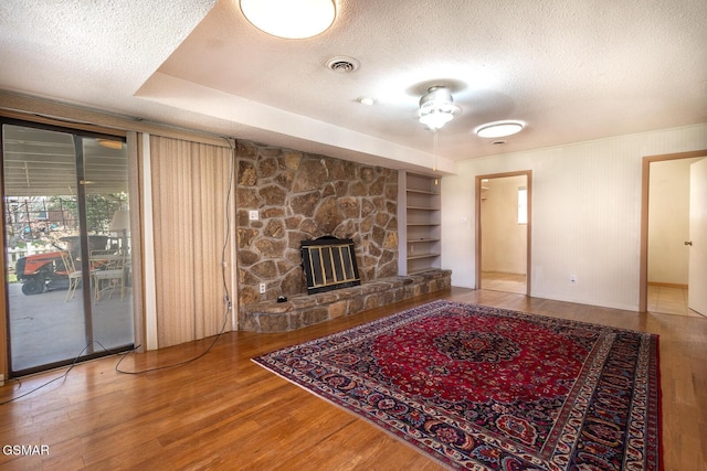 unfurnished living room featuring visible vents, built in shelves, a textured ceiling, and wood finished floors