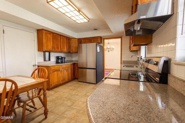 kitchen featuring brown cabinetry, an inviting chandelier, a sink, under cabinet range hood, and appliances with stainless steel finishes