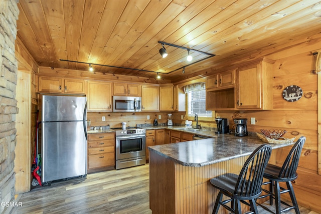 kitchen with appliances with stainless steel finishes, light wood-style floors, a sink, wooden ceiling, and a peninsula