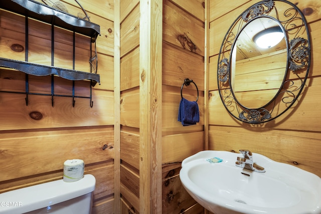 half bath with toilet, wood walls, and a sink