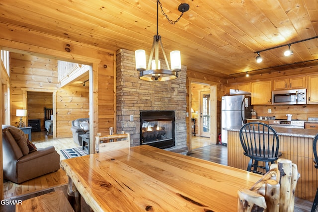 interior space featuring wooden ceiling, hardwood / wood-style flooring, a stone fireplace, wood walls, and a notable chandelier