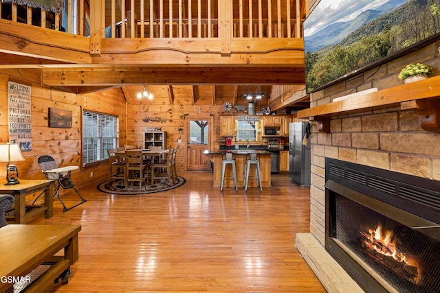 living room featuring a high ceiling, light hardwood / wood-style flooring, a stone fireplace, and wood walls