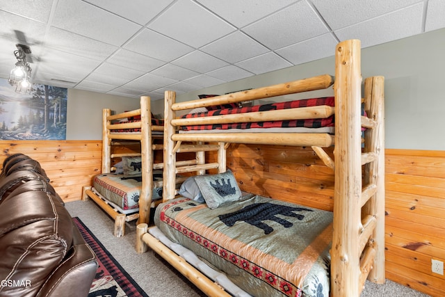 carpeted bedroom featuring a drop ceiling and wood walls