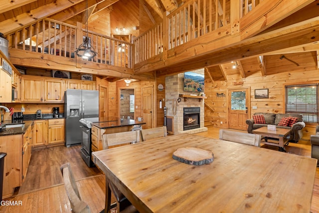 dining space with a fireplace, beam ceiling, high vaulted ceiling, and wooden walls