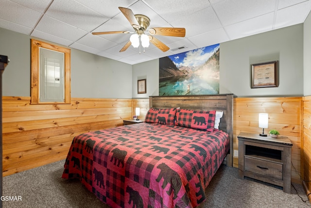 bedroom with ceiling fan, a drop ceiling, carpet floors, and wooden walls