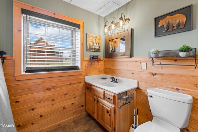 bathroom featuring tile patterned flooring, vanity, toilet, and wooden walls