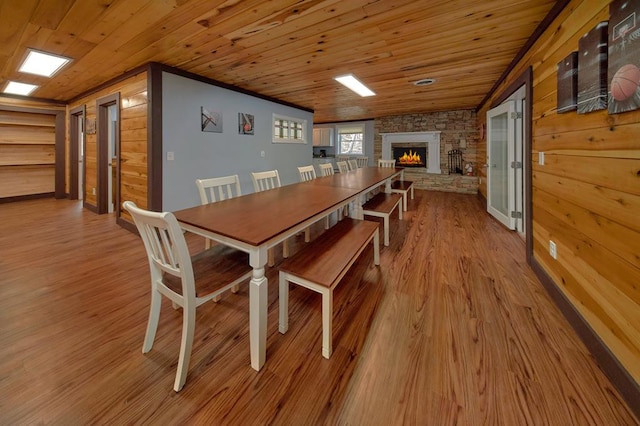 dining area with a stone fireplace, wooden walls, wood ceiling, and wood finished floors