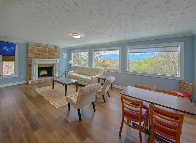 living area with baseboards, a stone fireplace, wood finished floors, and crown molding