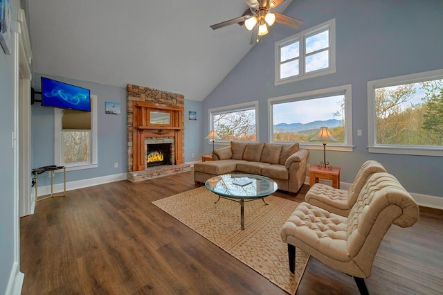 living room with baseboards, ceiling fan, a stone fireplace, wood finished floors, and high vaulted ceiling