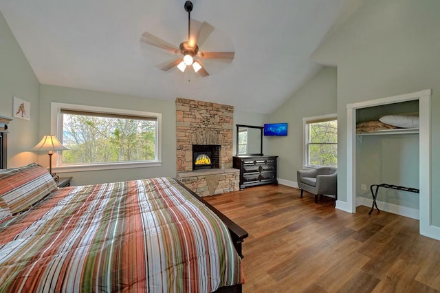 bedroom with a stone fireplace, multiple windows, wood finished floors, and baseboards
