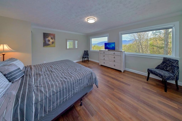 bedroom with ornamental molding, a textured ceiling, baseboards, and wood finished floors
