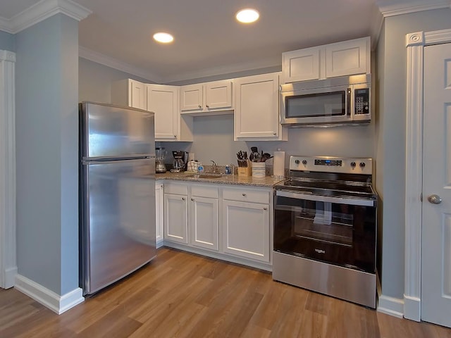 kitchen featuring crown molding, light wood-type flooring, appliances with stainless steel finishes, white cabinetry, and a sink