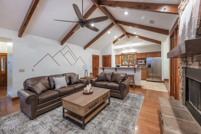 living room with a stone fireplace, high vaulted ceiling, beamed ceiling, ceiling fan, and light hardwood / wood-style floors