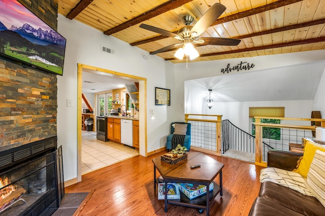 living room featuring light wood-type flooring, lofted ceiling with beams, a stone fireplace, and wood ceiling