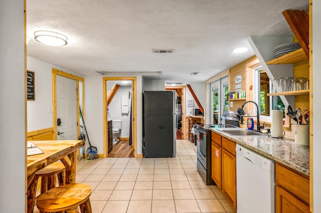 kitchen with dishwasher, sink, light stone countertops, a textured ceiling, and stainless steel refrigerator