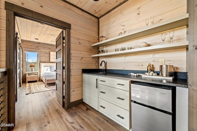 bar featuring wooden ceiling, wood finished floors, freestanding refrigerator, wood walls, and a sink