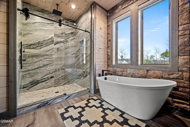 full bathroom featuring wood finished floors, a soaking tub, a marble finish shower, and wooden walls