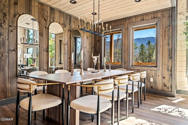 dining area with a chandelier, wooden ceiling, wood finished floors, and wooden walls