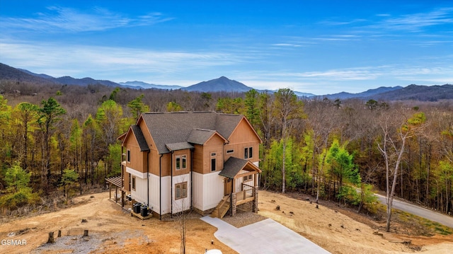 view of front facade featuring a shingled roof, a mountain view, and a forest view