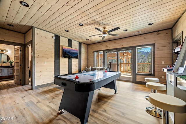 rec room featuring light wood-style floors, wooden ceiling, a ceiling fan, and wooden walls