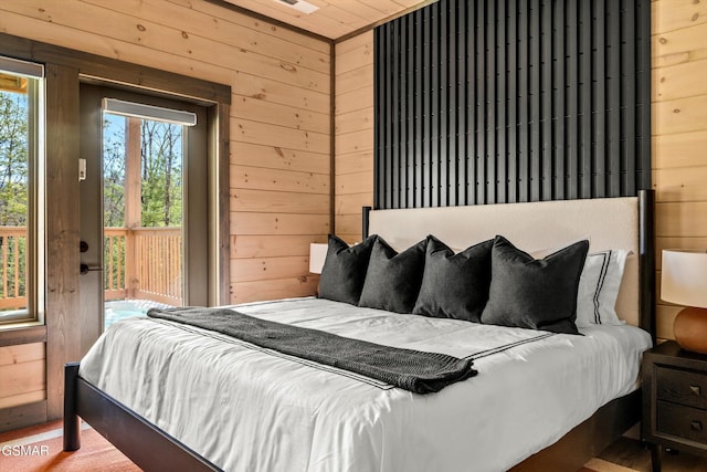 bedroom featuring access to outside, multiple windows, and wood walls