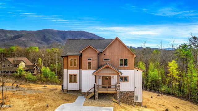 view of front of home with a shingled roof, a mountain view, and a view of trees